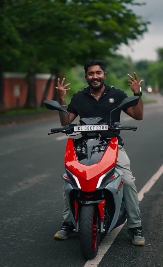 Creator sitting on a red TVS NTORQ scooter, smiling at camera